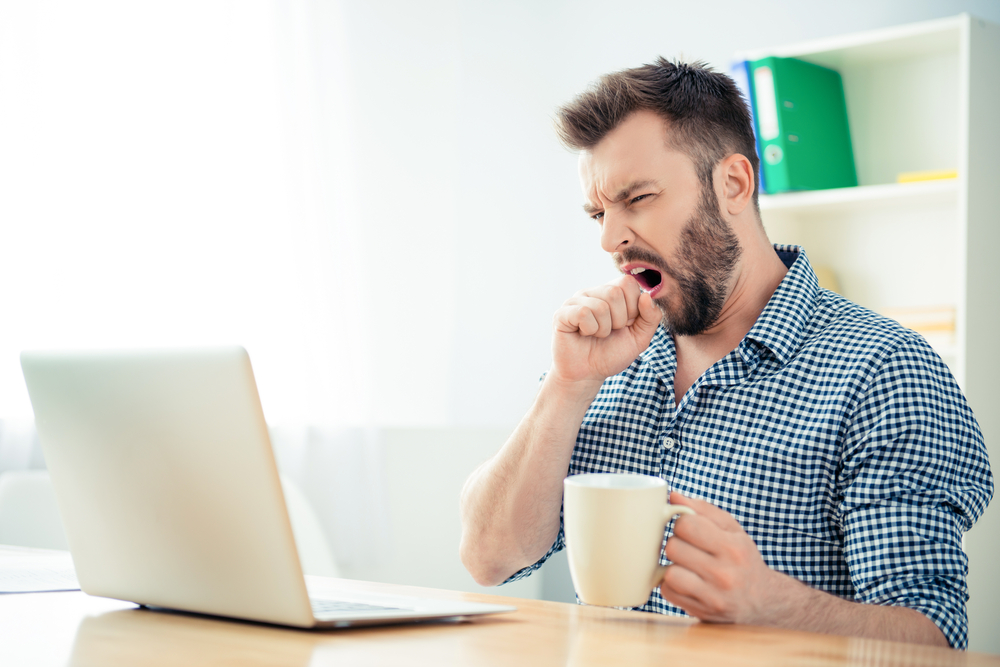 Young businessman yawning and drinking coffee to be energetic